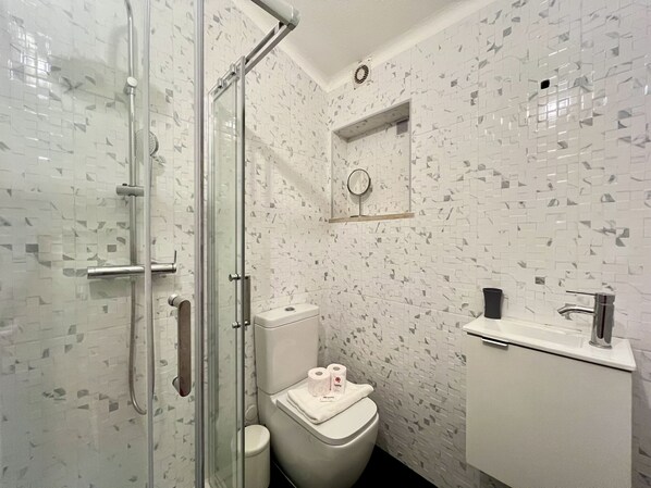A bathroom with a glass-enclosed shower, a toilet, and a sink with a mirror above it.