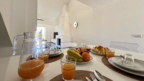 Aamiaispöytä on katettu lautasilla, laseilla ja kannulla, jossa on appelsiinimehua.