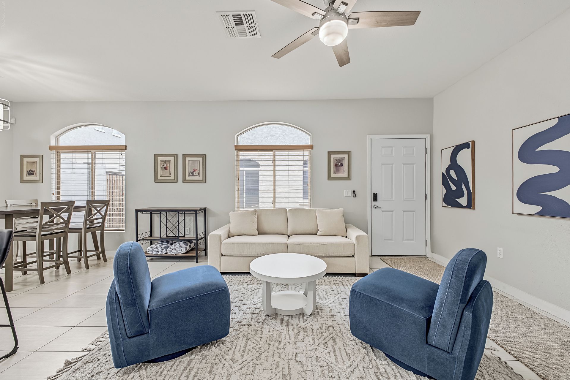 Un salon comprenant un canapé, deux fauteuils, une table basse, une table à manger avec des chaises et un ventilateur de plafond.