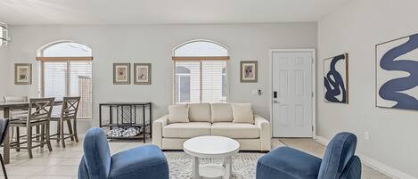 Un salon comprenant un canapé, deux fauteuils, une table basse, une table à manger avec des chaises et un ventilateur de plafond.