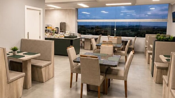 A modern dining area with a central table surrounded by chairs, a kitchen in the background, and a view of the cityscape through large windows. - Di Palazzo (Ametista do Sul)