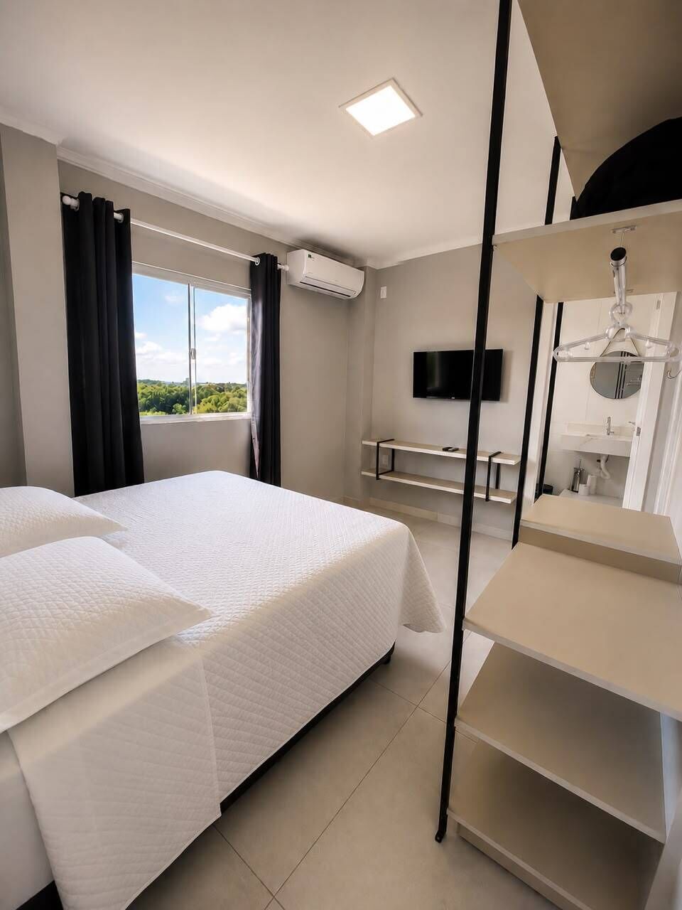 A hotel room with a bed, a TV, a desk, and a window with curtains.