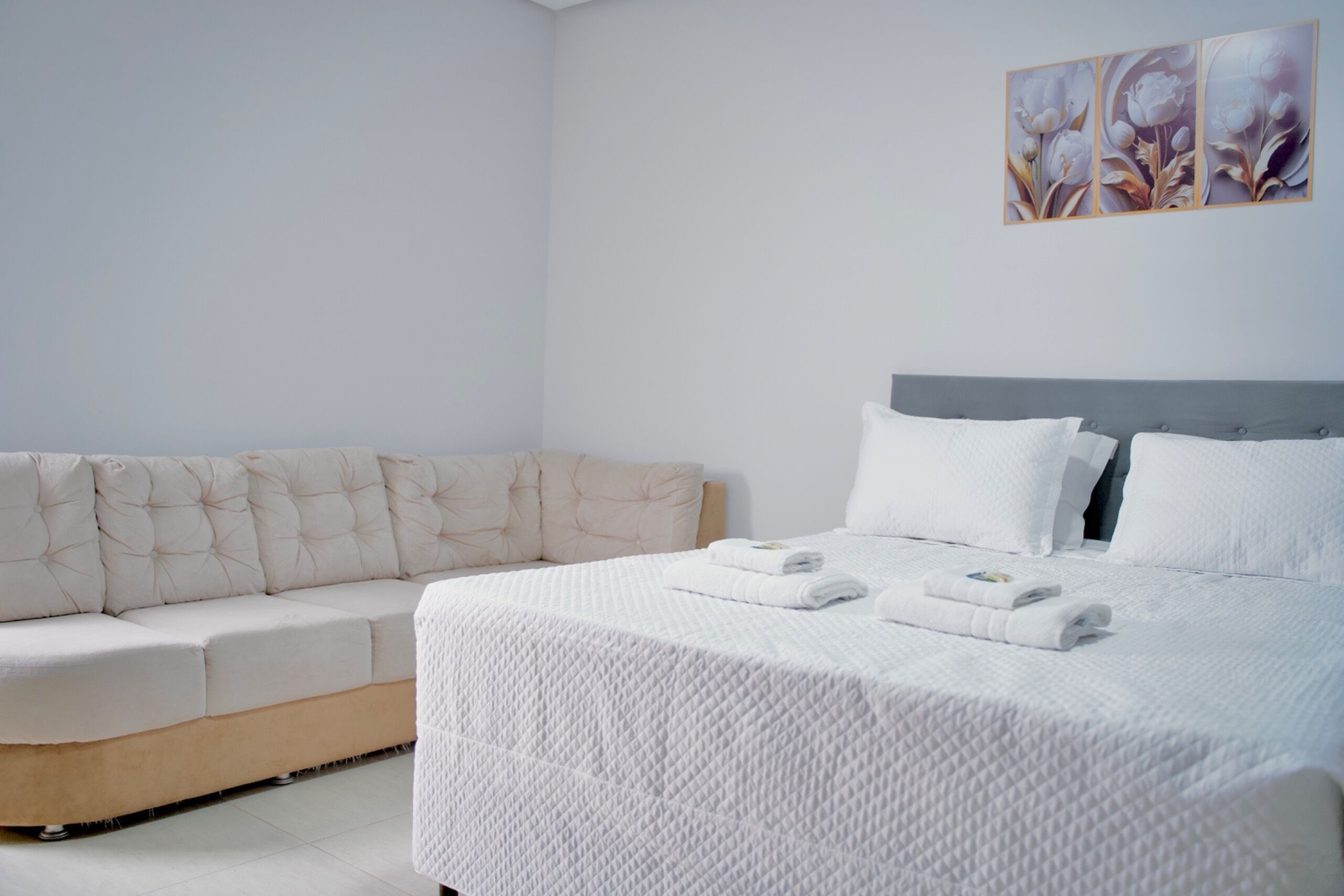 A modern bedroom with a large bed, a sofa, and a wall-mounted artwork.