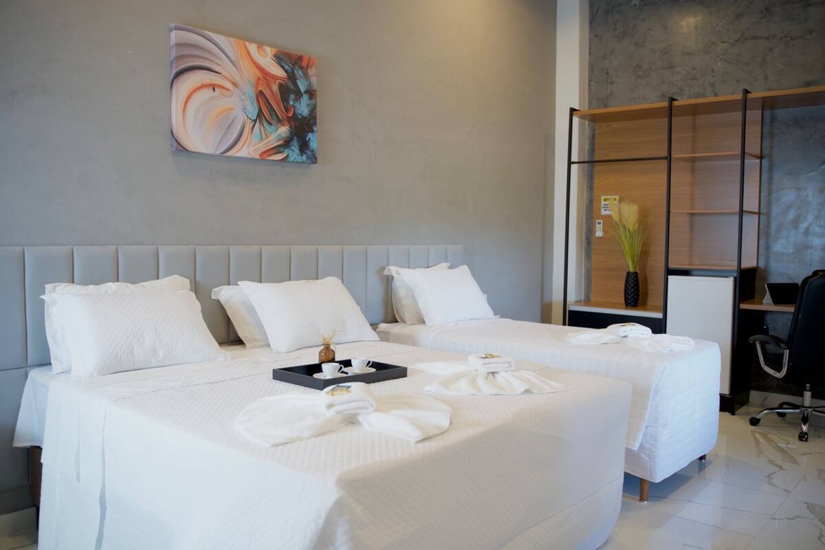 Ein Hotelzimmer mit zwei Betten, einem Bild an der Wand, einem Schreibtisch mit einer Vase und einem Sessel.