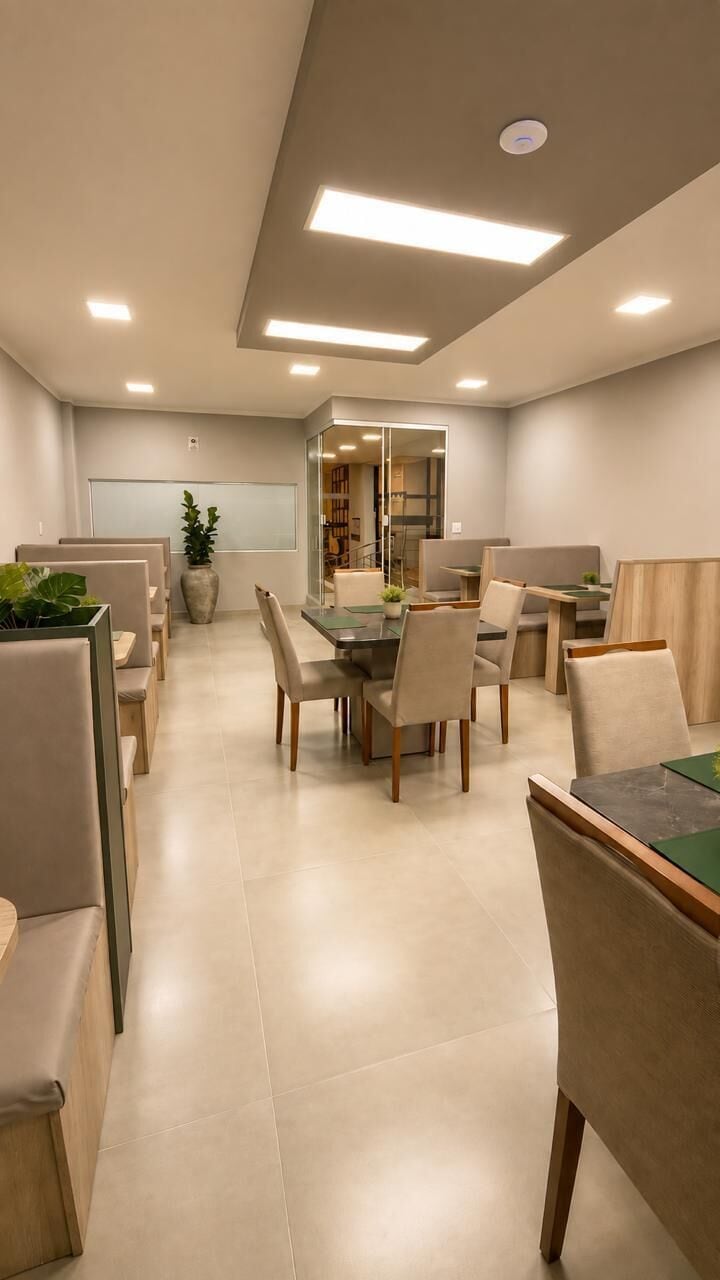 A modern dining area with a central table surrounded by chairs, a whiteboard on the wall, and a potted plant.