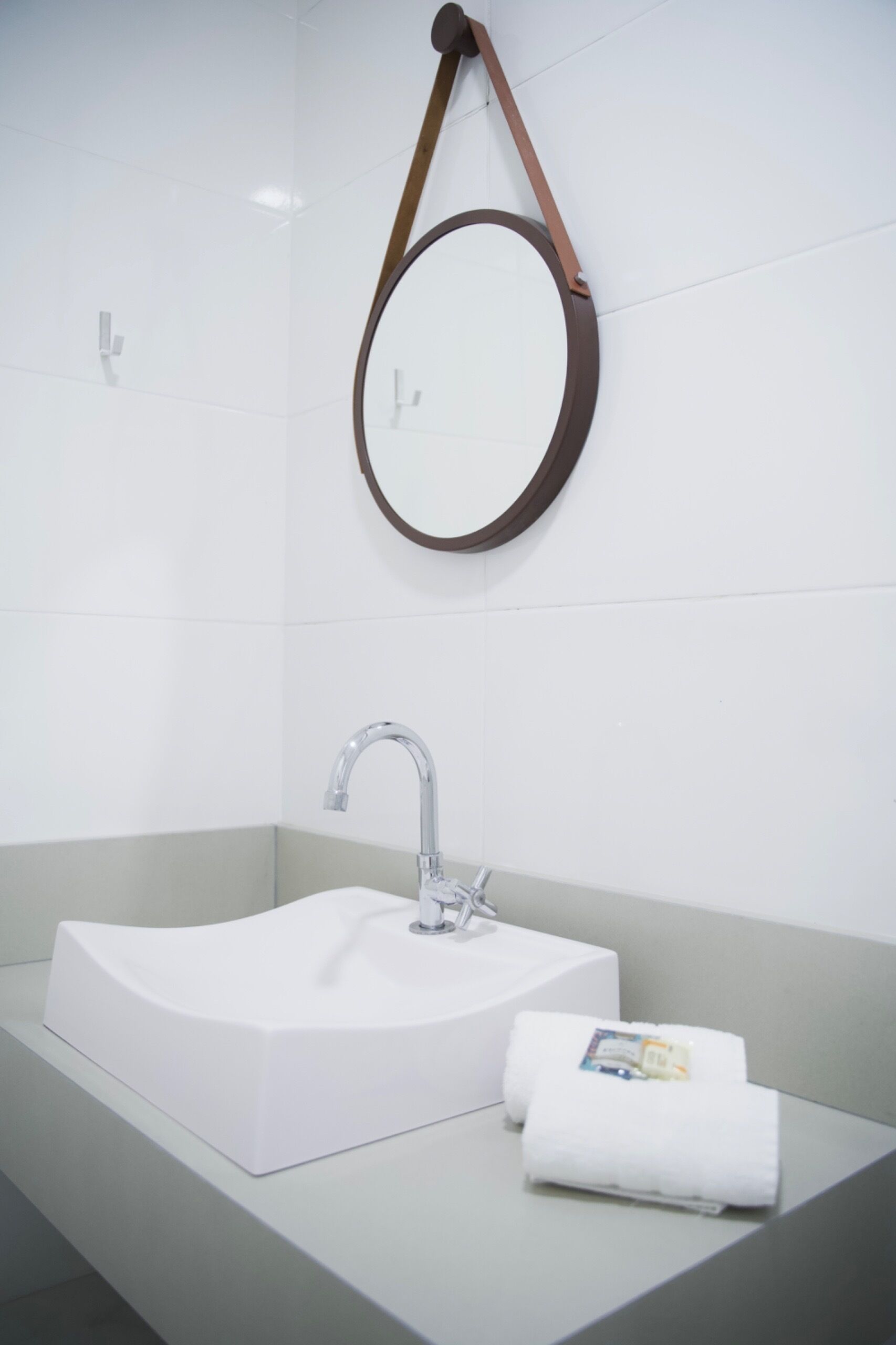 Un baño moderno con un lavabo blanco, un espejo redondo y un perchero para toallas.