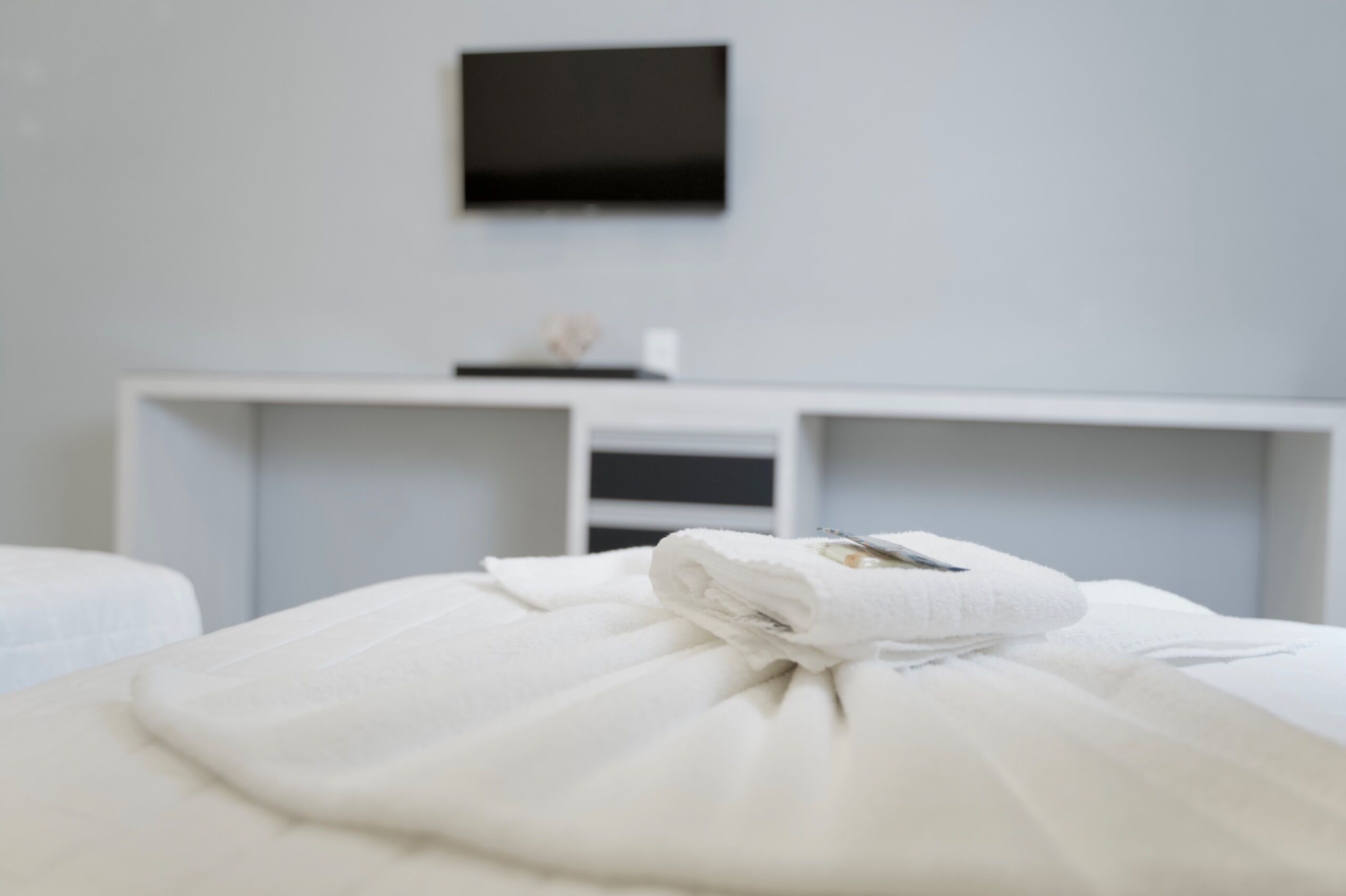Une chambre d’hôtel avec un lit, un téléviseur à écran plat fixé au mur et un bureau blanc agrémenté d’un petit objet décoratif.
