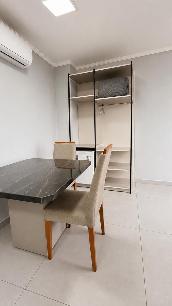 Une chambre moderne équipée d’une table à manger, de chaises, d’une armoire intégrée et d’un climatiseur blanc.