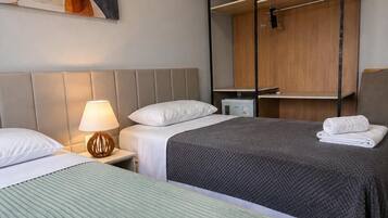 Hotellihuone, jossa on kaksi sänkyä, puinen hyllykkö ja taulu seinällä.