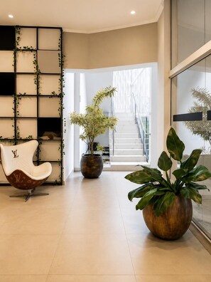 Un intérieur moderne avec une chaise blanche, une grande plante en pot et un escalier menant à un espace lumineux.