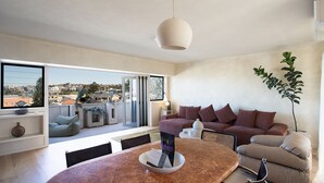 Een moderne woonkamer met een bank, een eettafel en uitzicht op de stad door grote ramen.