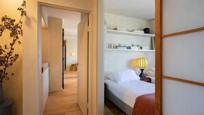 Een hotelkamer met een bed, nachtkastje, lamp en planken met boeken en decoratieve objecten.