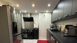 A modern kitchen with stainless steel appliances, a red patterned mat, and grey cabinets.