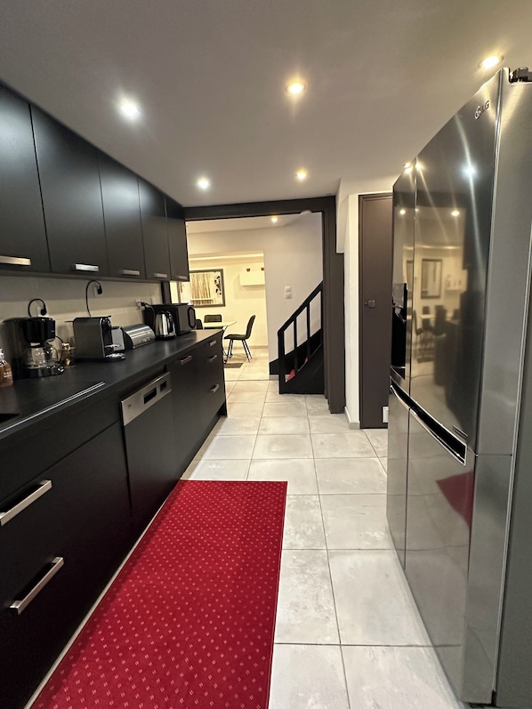 A modern kitchen with dark cabinets, a stainless steel refrigerator, and a red patterned rug.
