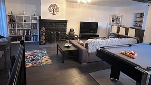 A modern living room with a pool table, a fireplace, a TV, and a bookshelf.