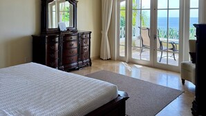 A bedroom with a large bed, a dresser, a ceiling fan, and a view of the outdoors through a sliding glass door. - Celebration Villa with Private Pool & Sunset Views (Mount Standfast)