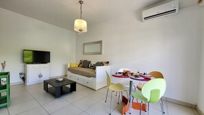 Un espacio habitable compacto con sofá, mesa de comedor, sillas, televisor y unidad de aire acondicionado.
