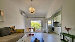 Una sala de estar moderna con un sofá, una mesa de comedor y sillas. Hay una zona de cocina con armarios y una escultura decorativa de un pájaro.