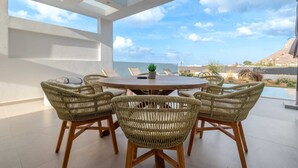 Una mesa redonda de madera con sillas de mimbre, una planta en maceta y vistas a una piscina y montañas.