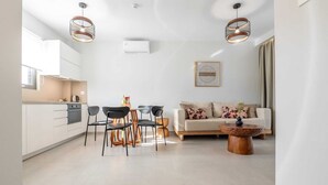 Un apartamento moderno con cocina, comedor y sala de estar. Presenta una paleta de colores blanca, una mesa de centro redonda de madera y un sofá con cojines estampados.