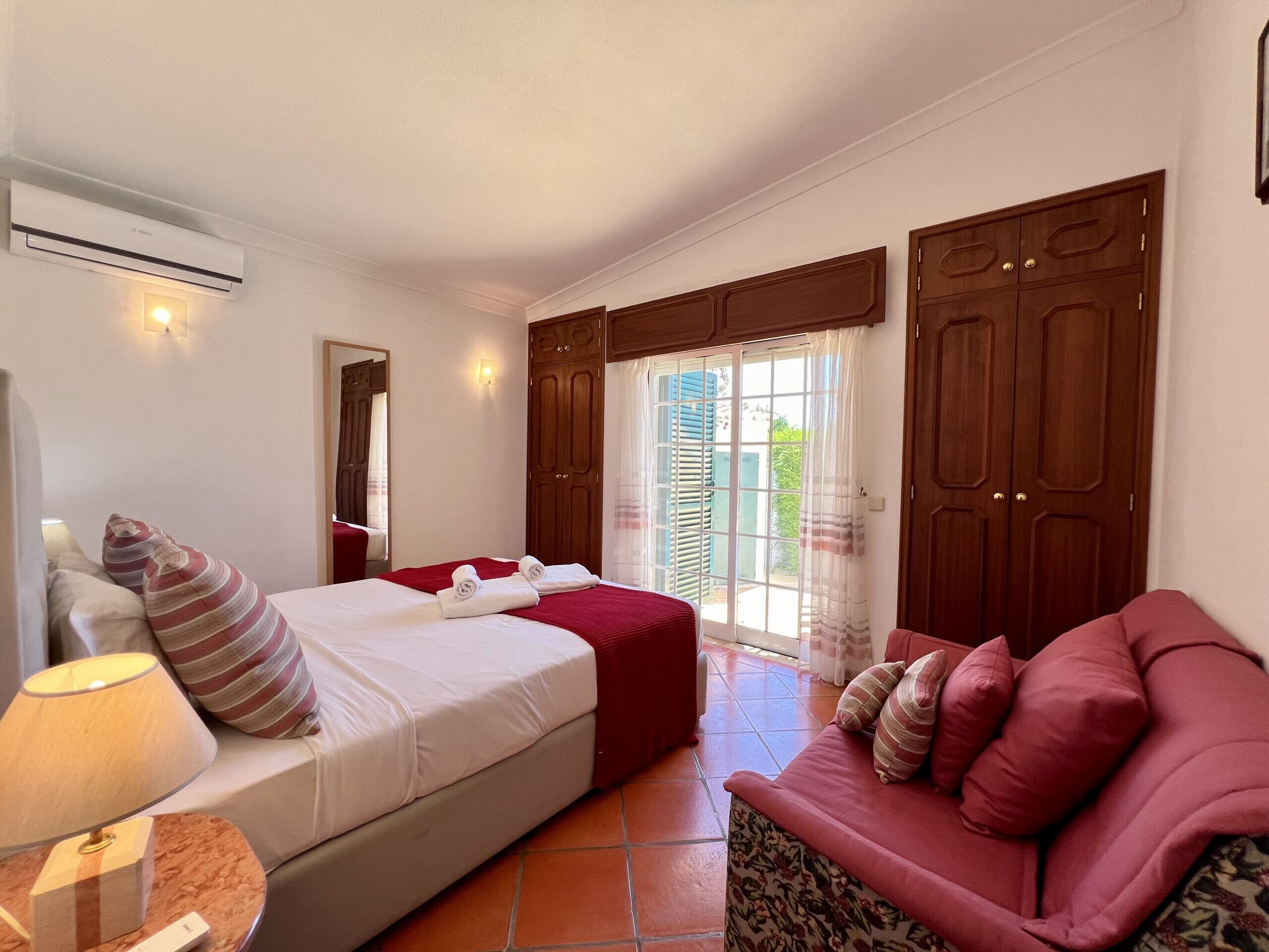 A hotel room with a bed, a sofa, a lamp, and a window with curtains.