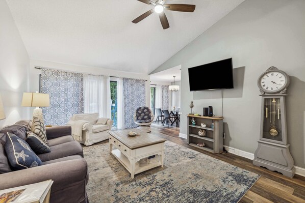 A living room with a sofa, coffee table, TV, clock, and a ceiling fan.