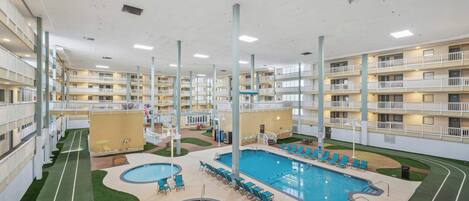 Un hotel de varios niveles con una piscina central, varios balcones y un césped bien cuidado.