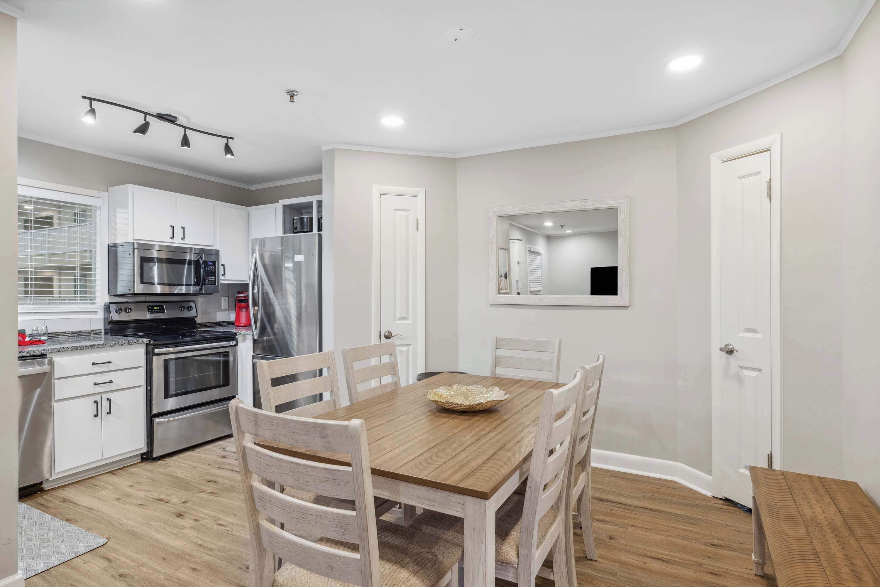 A modern kitchen with white cabinets, stainless steel appliances, and a wooden dining table with chairs.