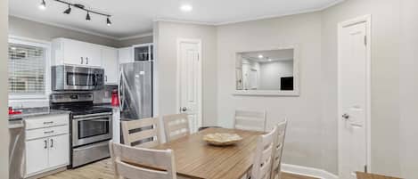 A modern kitchen with white cabinets, stainless steel appliances, and a wooden dining table with chairs.