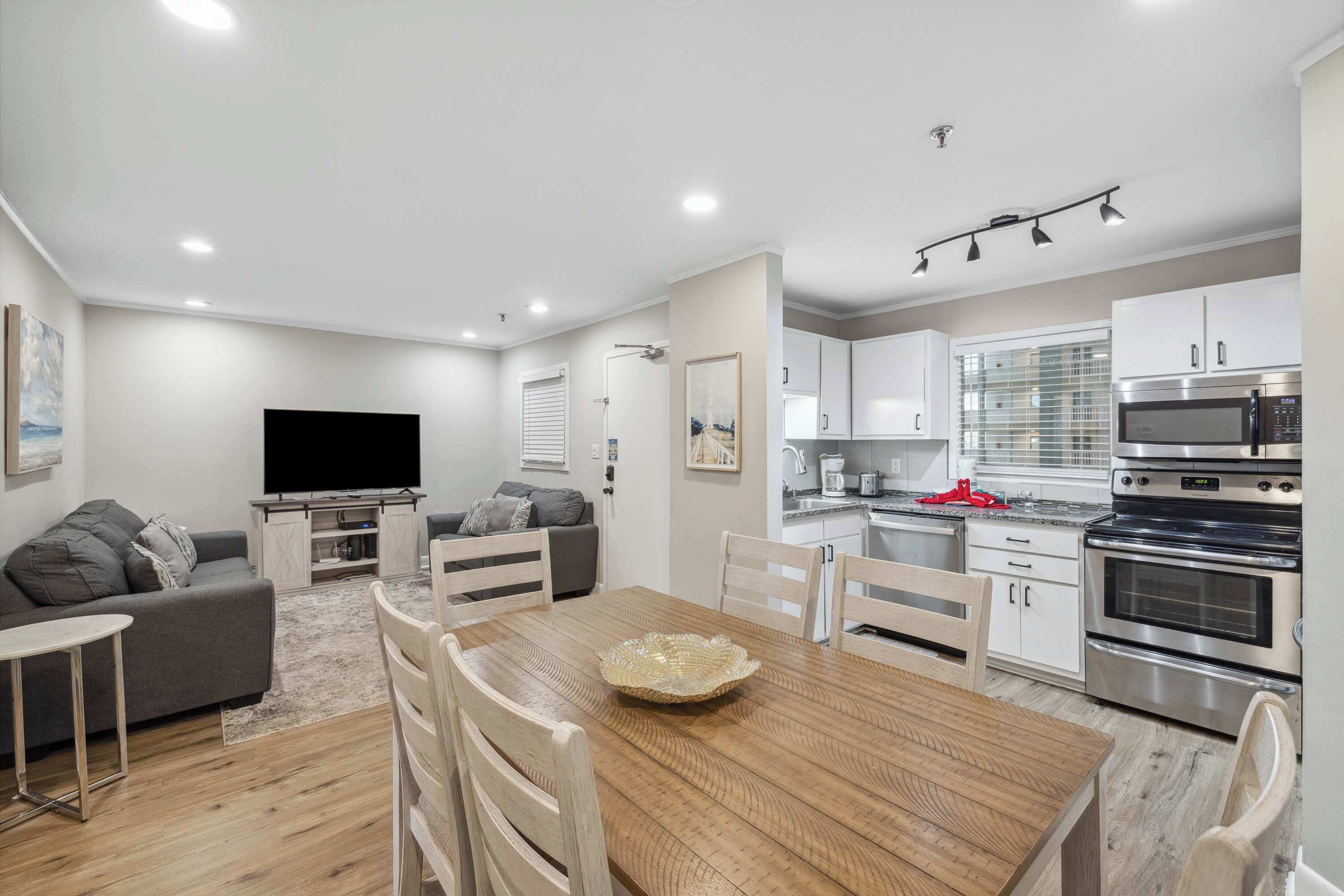 A modern living room with a flat-screen TV, grey sofa, and a dining area with a wooden table and chairs.