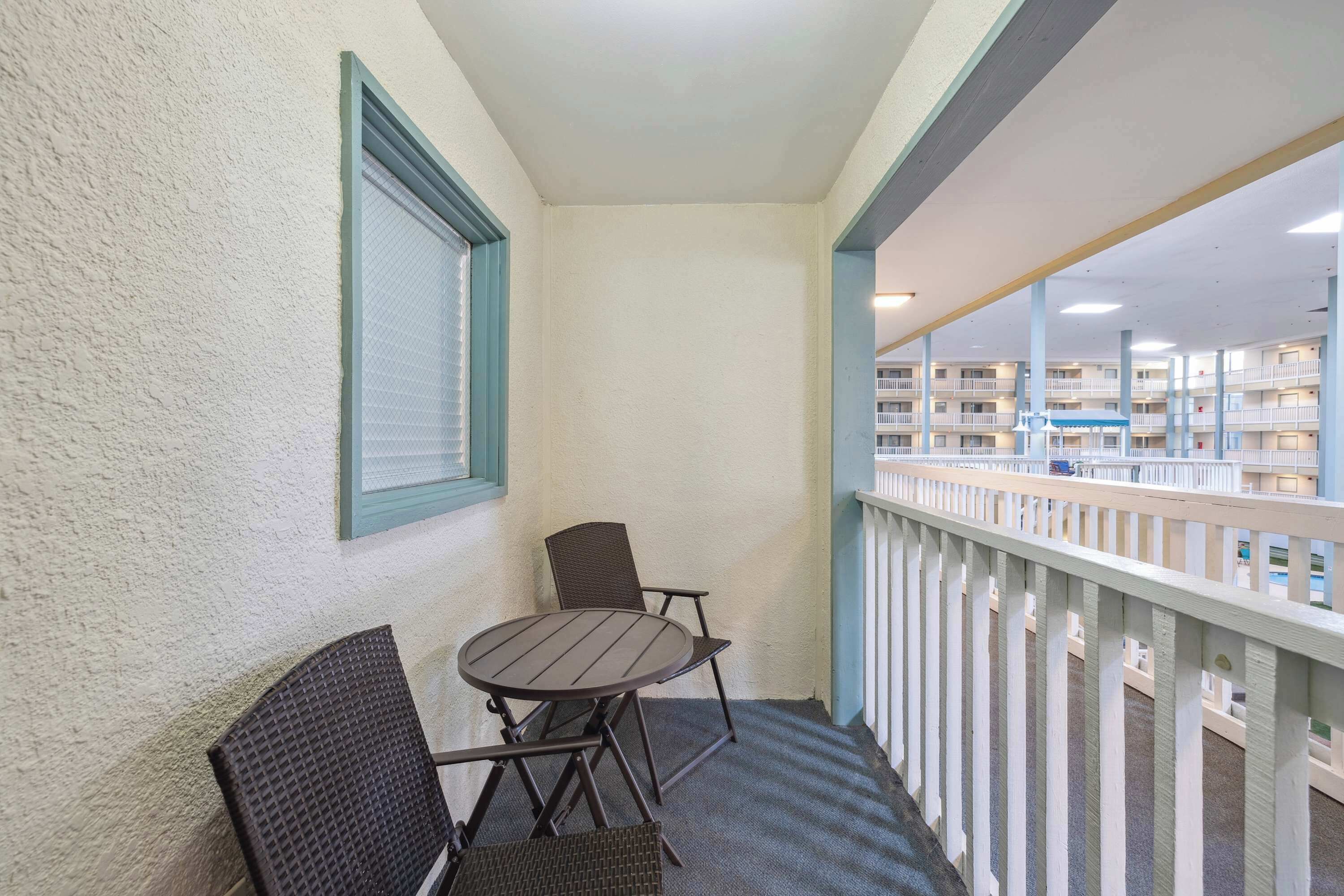 Un balcone con tavolo e sedie, una finestra con cornice blu e vista su un edificio con balconi.