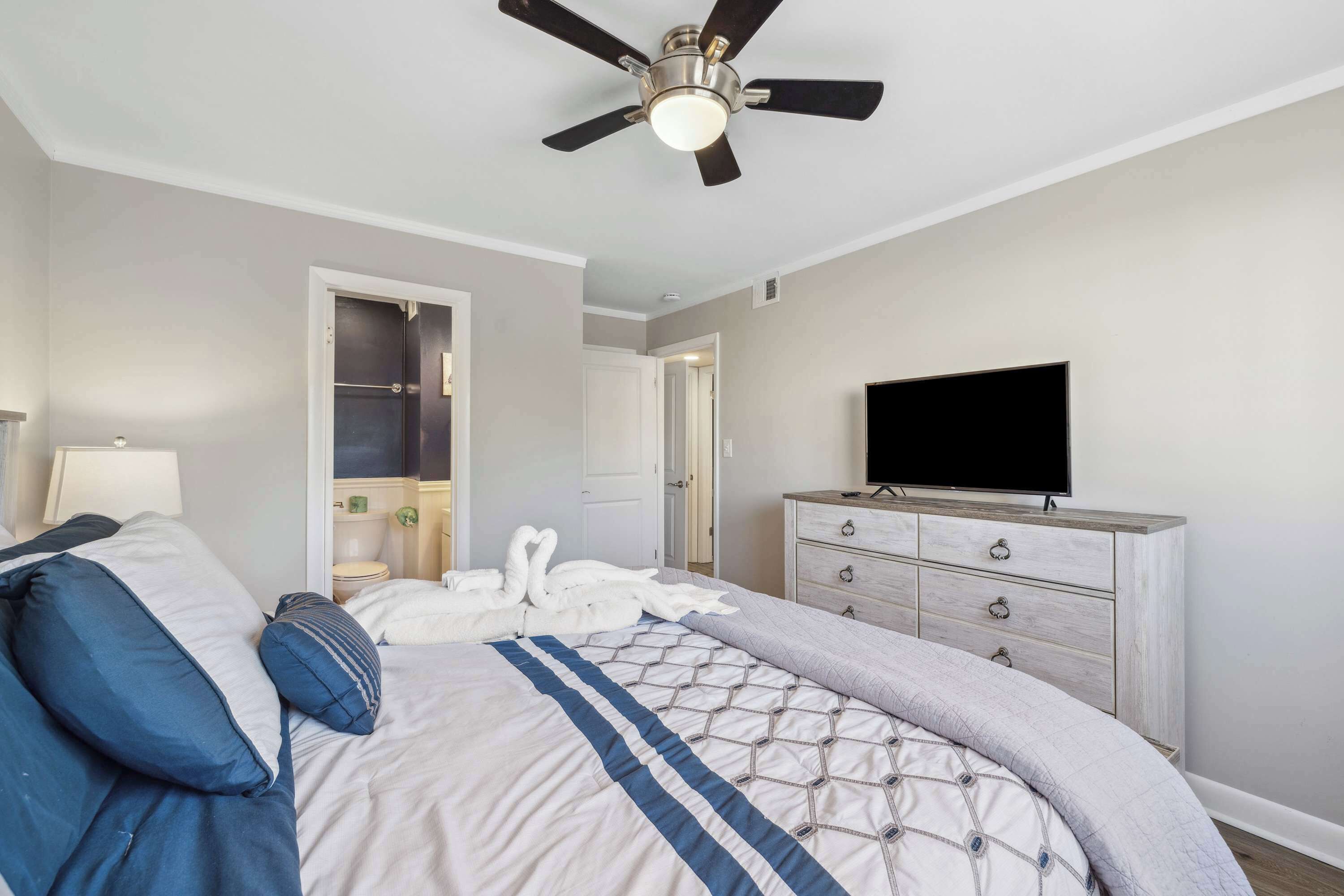 Ein Schlafzimmer mit Bett, Deckenventilator, Schminktisch und Fernseher.