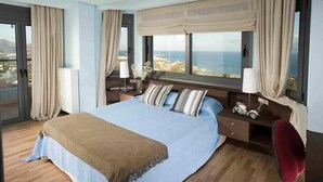 Ein geräumiges Schlafzimmer mit einem großen Bett, einem Nachttisch, einem Sessel und Meerblick.