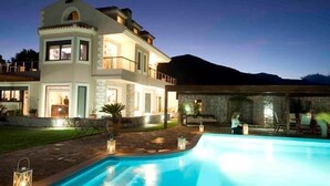 Ein zweigeschossiges Haus mit Swimmingpool, Naturstein-Fassade und einem Berg im Hintergrund.