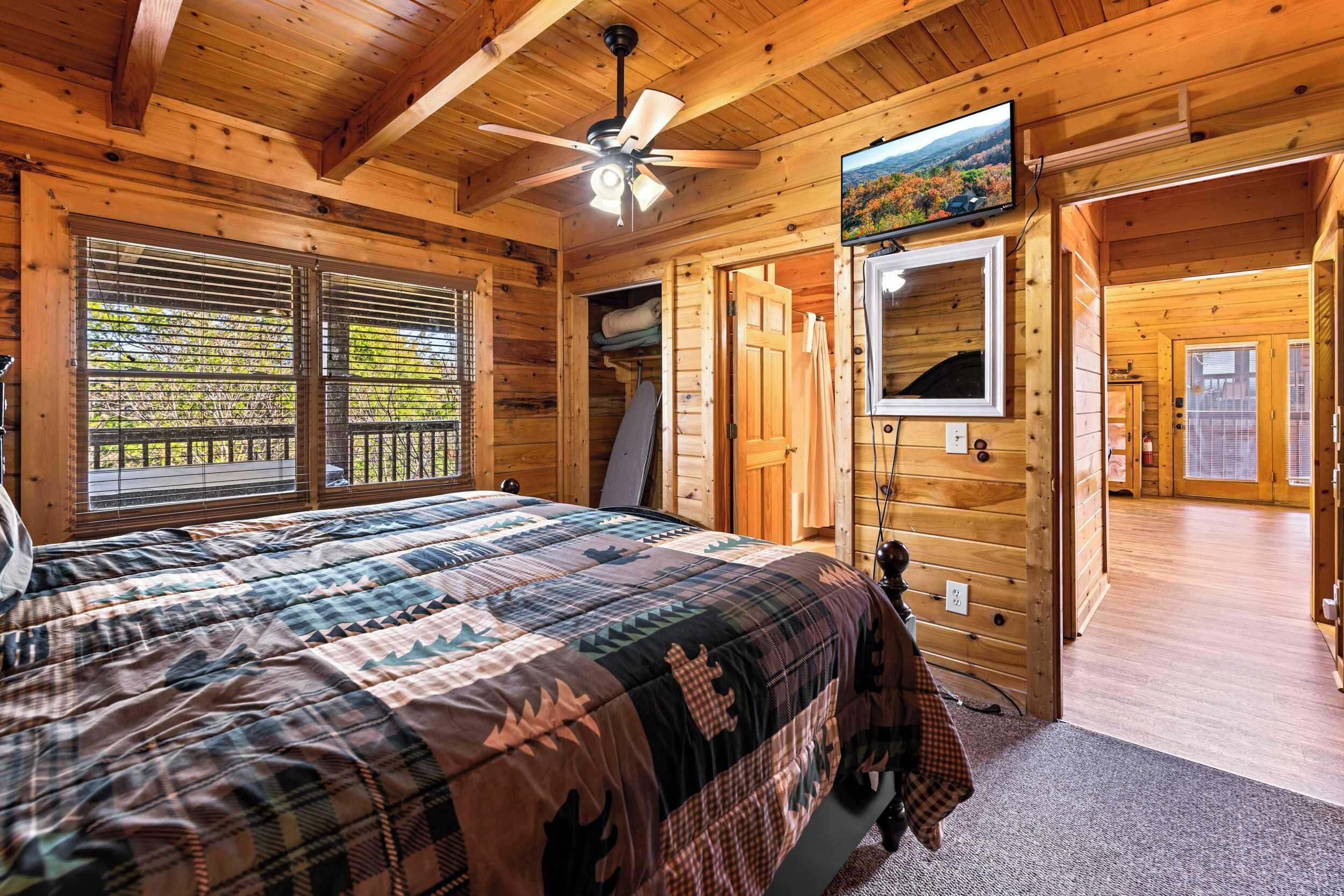 Une chambre dans un chalet en bois, avec un lit, un ventilateur de plafond, une télévision et une fenêtre avec des stores.