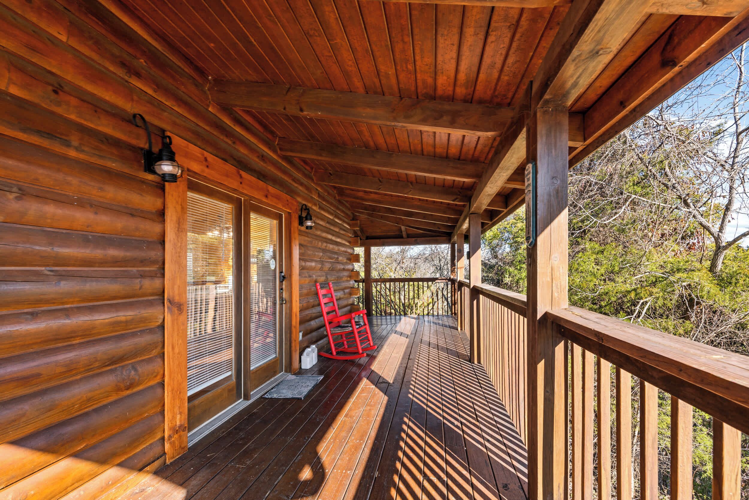 A wooden deck with a red chair, a wooden railing, and a view of trees.