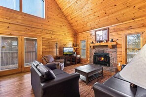 A log cabin interior with a fireplace, leather sofas, a television, and a stone wall.