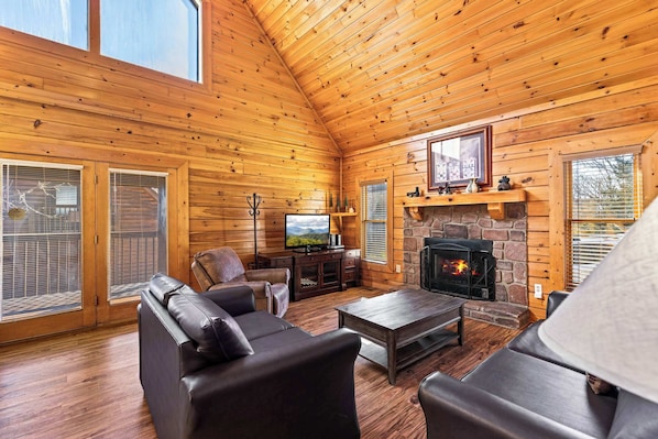 A log cabin interior with a fireplace, leather sofas, a television, and a stone wall.