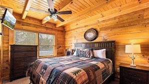 Un dormitorio de cabaña de madera con cama, cómoda, mesita de noche y ventilador de techo.