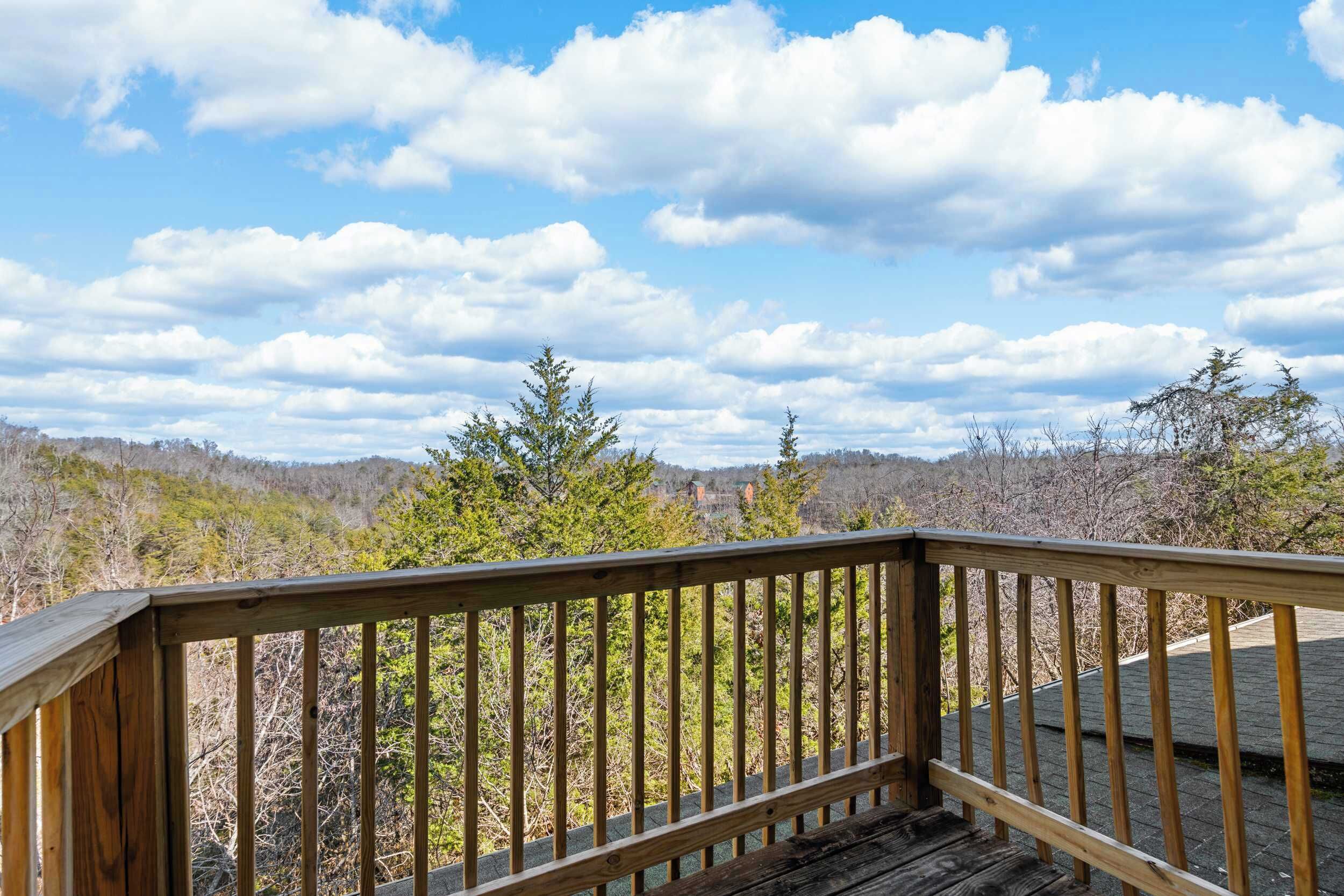 A wooden deck with a railing overlooking a forested landscape.