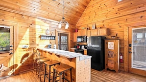 Una cabaña de madera con cocina que incluye una zona de bar, armarios de madera y un refrigerador negro.