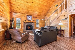 A log cabin interior with a fireplace, leather sofas, and a staircase.