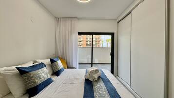A hotel room with a bed, a view of a building through a glass door, and a ceiling light.