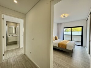 Ein modernes Schlafzimmer mit großem Fenster, einem Bett und einem Badezimmer mit Spiegel und Waschbecken.