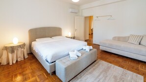 A modern bedroom with a large bed, a sofa, and a small table with a lamp. - Residenza Serego - affaccio scavi Romani (Verona)