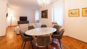 A dining area with a round table and six chairs, a sofa, a TV, and a chandelier. - Residenza Serego - affaccio scavi Romani (Verona)