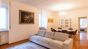 A living room with a sofa, a dining table with chairs, a chandelier, and a framed picture on the wall. - Residenza Serego - affaccio scavi Romani (Verona)