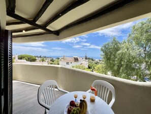Enjoy a seaside view from this balcony with a table set for a refreshing meal.