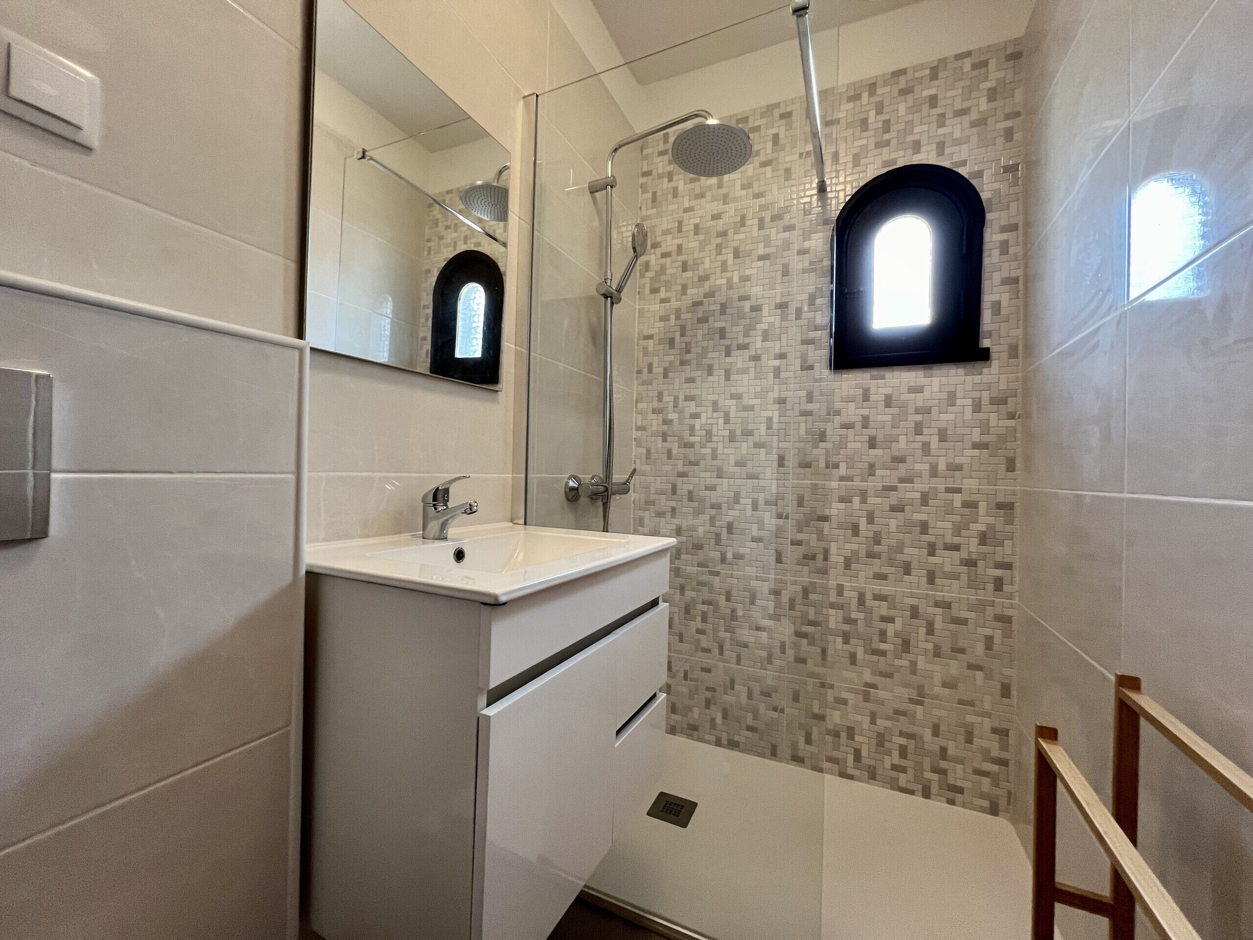 Une salle de bain moderne avec un meuble-lavabo blanc, une cabine de douche en verre et un mur recouvert de carreaux formant un motif géométrique.