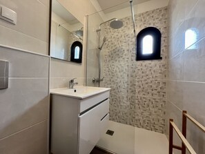 Un bagno moderno con un mobile lavabo bianco, una cabina doccia in vetro e una parete rivestita di piastrelle con motivo geometrico.